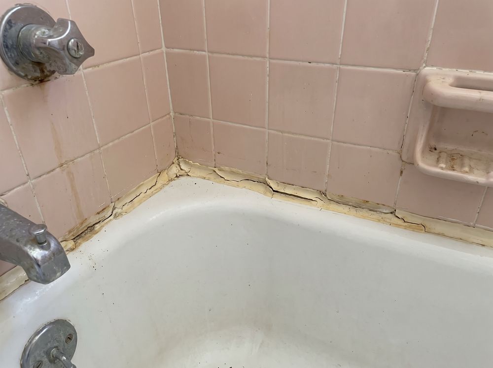 A bathtub corner where the old caulk has cracked away from pink tile