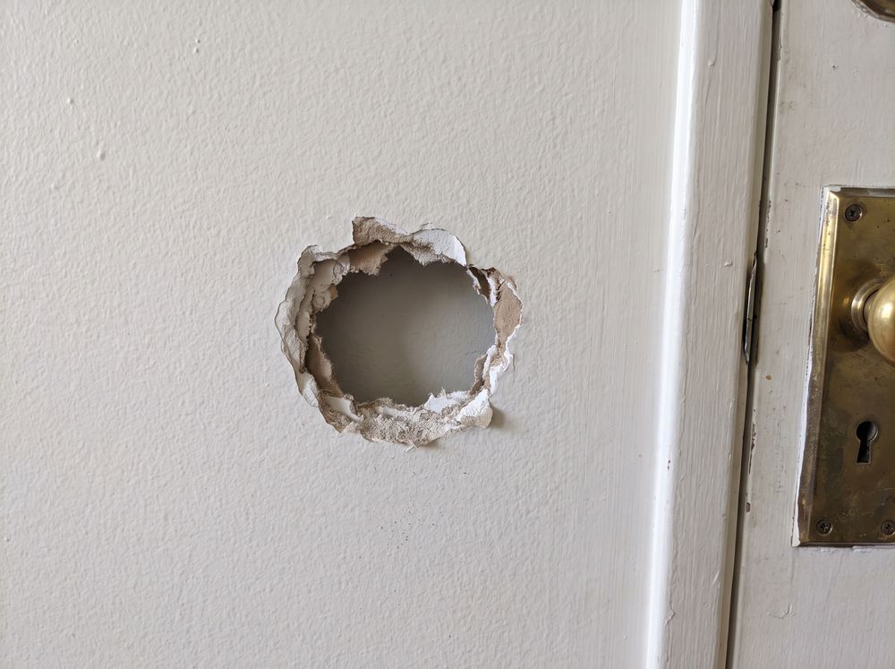 A fist-sized hole in a painted drywall wall behind a door
