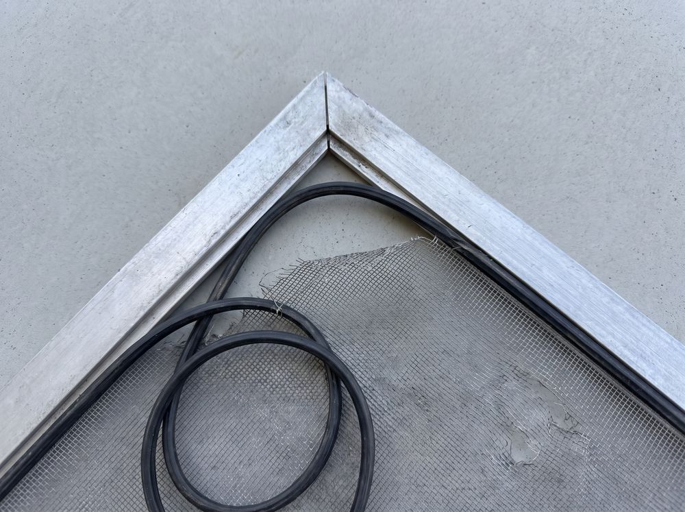 The corner of an aluminum window screen frame with the spline out and the mesh torn