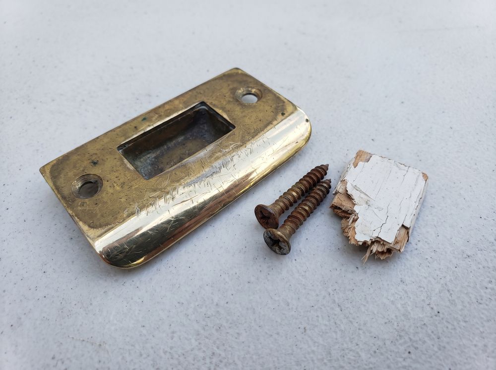 A worn brass door strike plate with its two screws